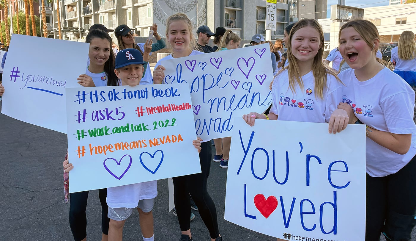 Group of people holding supportive signs about mental health awareness during an outdoor event.