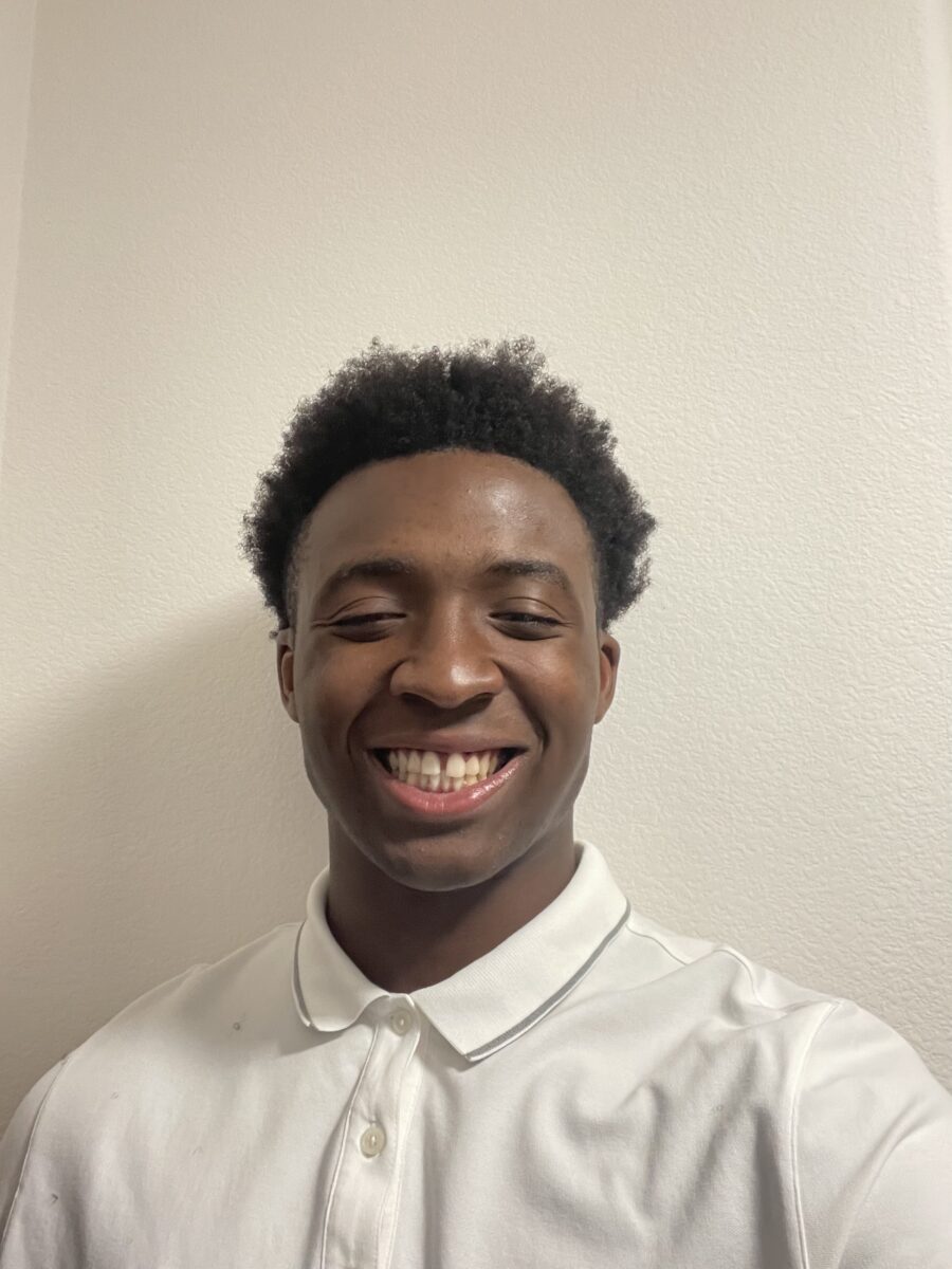 A young man in a white polo shirt smiling in front of a plain white wall.