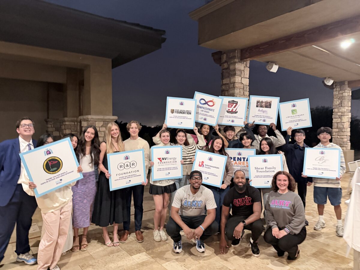 Group of smiling people hold large sponsor signs while posing together outside in the evening.